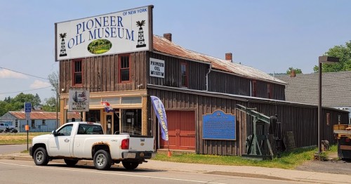 A rustic building with a sign reading "Pioneer Oil Museum," featuring a pickup truck parked outside.