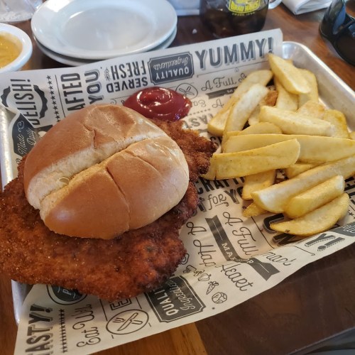 A crispy chicken sandwich on a bun with fries and ketchup on a patterned tray.