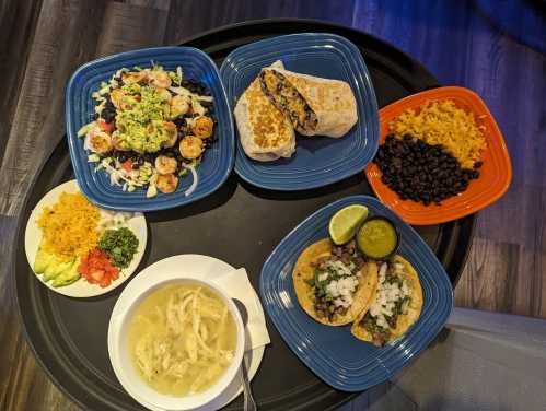 A tray with colorful plates of tacos, burrito, salad, rice, beans, and a bowl of soup.