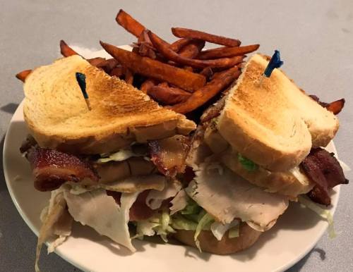 A stacked sandwich with turkey, bacon, and lettuce, served with a side of crispy sweet potato fries.