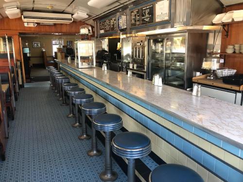 A retro diner interior featuring a long marble counter with blue stools and a view of the kitchen area.