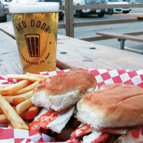 A glass of beer next to two sandwiches and fries on a wooden table with a checkered paper lining.