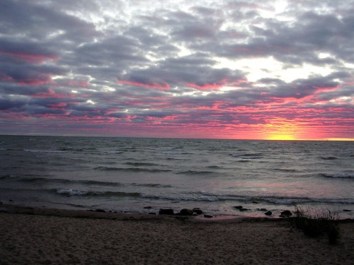 A serene beach scene at sunset, with vibrant pink and orange clouds reflecting over the calm water.