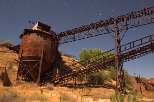 Rusty industrial structure with a tall metal framework and a large cylindrical tank, set against a starry night sky.