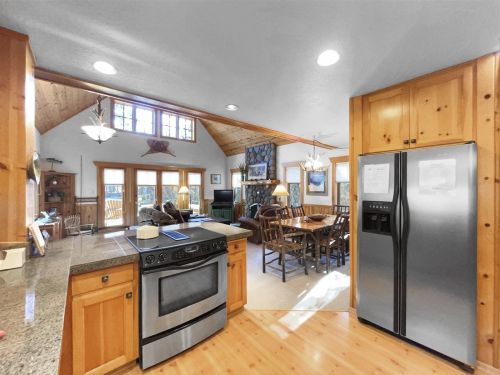 Cozy kitchen with wooden cabinets, stainless steel appliances, and a dining area featuring a stone fireplace and large windows.