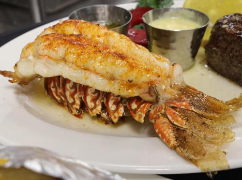 A beautifully plated lobster tail with a golden-brown sear, served with lemon and dipping sauce on a white plate.