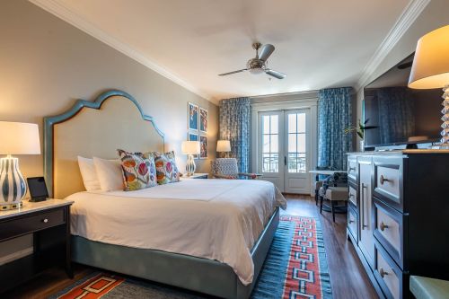 Cozy hotel room featuring a king bed, decorative pillows, a TV, and large windows with blue curtains.