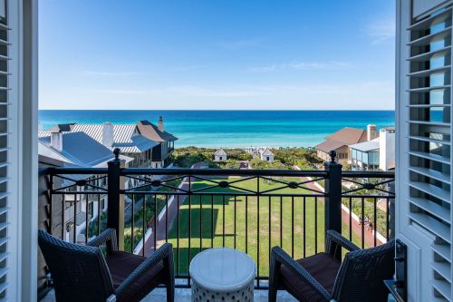 View from a balcony overlooking a serene beach and ocean, with green lawns and houses in the foreground.