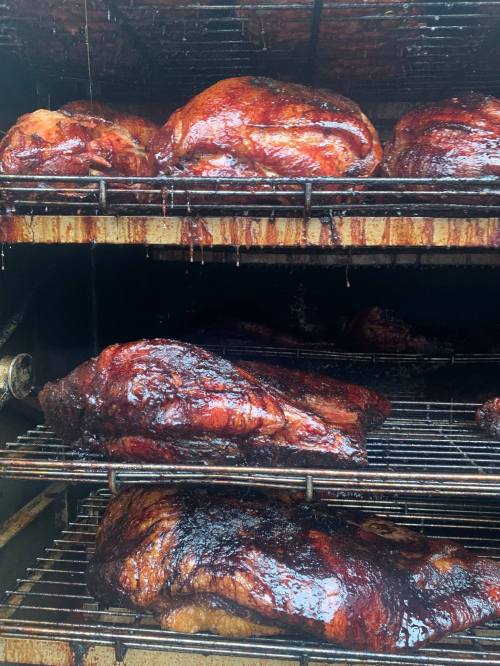 Smoked meats on racks in a smoker, glistening with a rich, dark glaze.