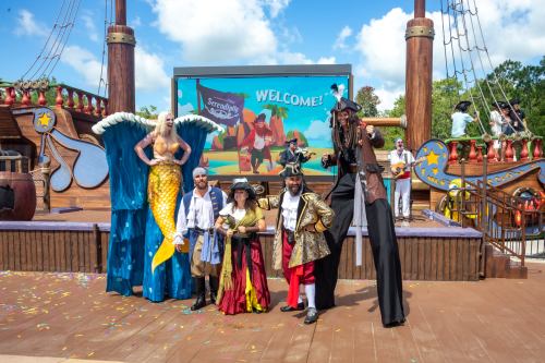 A colorful stage with performers in costumes, including a mermaid and pirates, welcoming guests at a themed event.