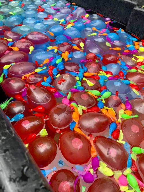 A colorful assortment of water balloons floating in a pool, surrounded by vibrant confetti-like decorations.