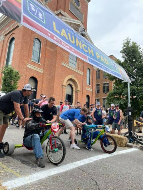Two racers in colorful go-karts prepare to start a race under a banner reading "LAUNCH PAD," with a crowd watching.