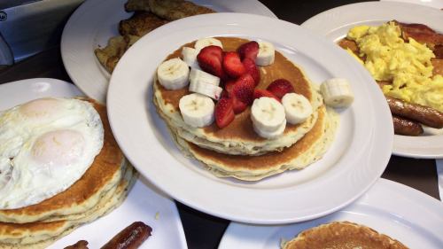 A stack of pancakes topped with sliced strawberries and bananas, served with eggs, sausage, and French toast.