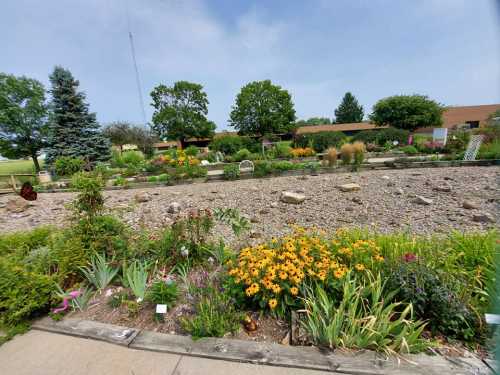 A vibrant garden filled with colorful flowers, rocks, and greenery under a clear blue sky.