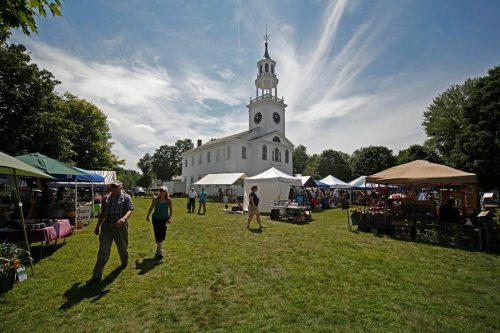 A vibrant outdoor market with tents and people, set against a historic church under a blue sky with clouds.