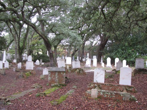A serene cemetery with white gravestones surrounded by trees and fallen leaves, creating a peaceful atmosphere.