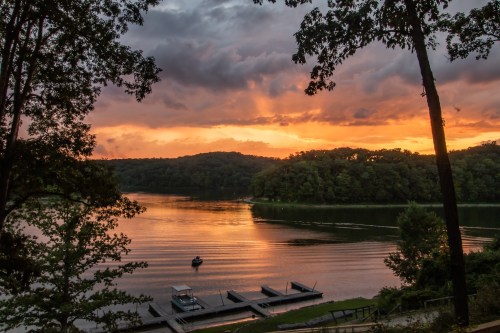 A serene lake at sunset, with vibrant orange skies and silhouettes of trees, reflecting on the calm water.