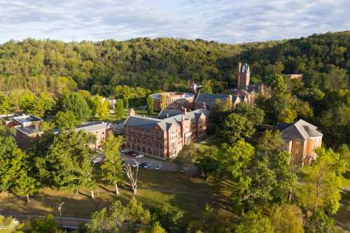 Aerial view of a college campus surrounded by trees and hills, featuring historic brick buildings and a clock tower.