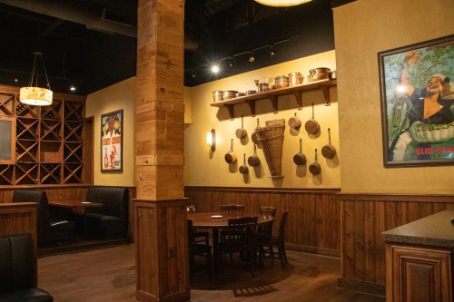 Cozy restaurant interior featuring wooden decor, a wine rack, and a wall display of pots and vintage posters.