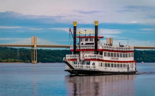 A steamboat sails on a river with a bridge in the background under a blue sky.