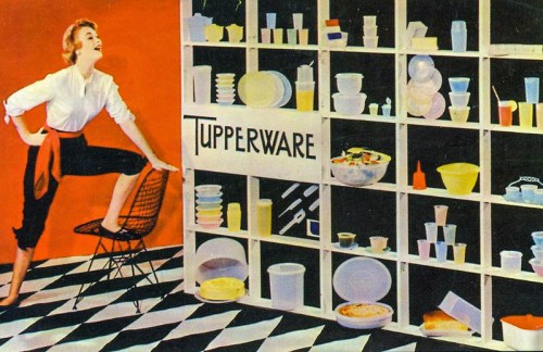 A woman poses playfully next to a colorful display of Tupperware containers on a black and white checkered floor.