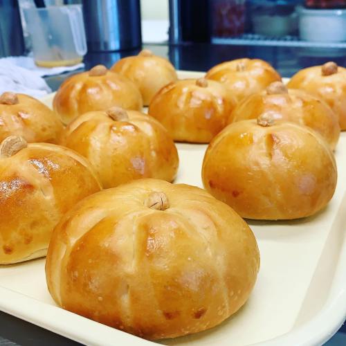A tray of golden-brown, round pastries with a shiny glaze and a small nut on top, arranged neatly.