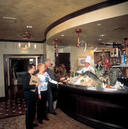 A couple interacts with a chef at a seafood display in an elegant restaurant, with a warm atmosphere and decor.