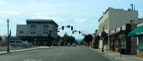 A quiet street scene with traffic lights, storefronts, and a clear sky in a small town.