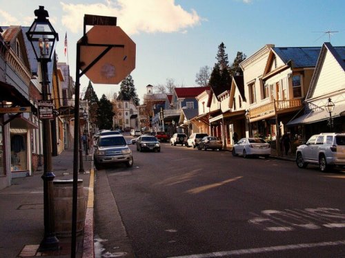 A quaint street lined with historic buildings, shops, and parked cars under a clear blue sky.