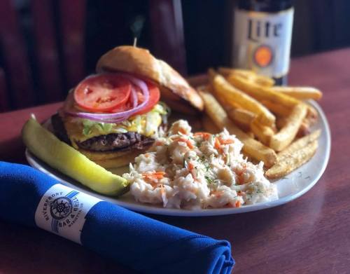 A plate featuring a burger with toppings, fries, coleslaw, a pickle, and a beer on the side.