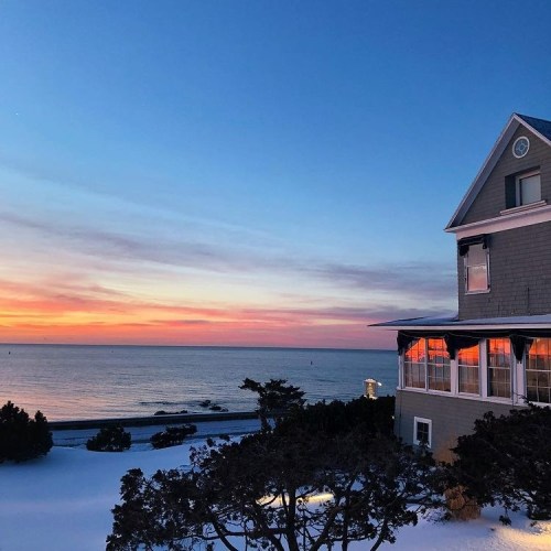 A serene beach scene at sunset, featuring a house by the shore and colorful skies reflecting on the water.