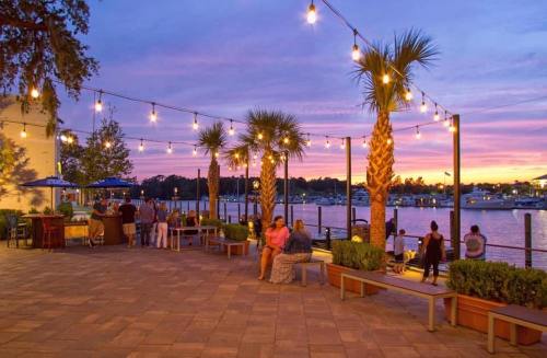 A vibrant sunset over a waterfront area with palm trees, string lights, and people enjoying the scenery.