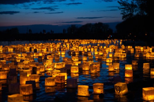 A serene scene of glowing lanterns floating on water at dusk, surrounded by a tranquil blue sky.