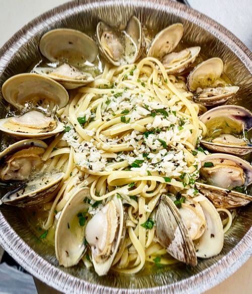 A silver tray filled with linguine pasta topped with clams, garlic, and herbs in a light broth.