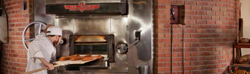 A baker places freshly baked bread into a large, brick oven.