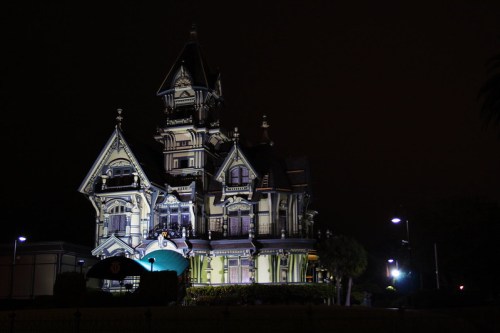 A large, ornate Victorian-style mansion illuminated at night, surrounded by dark skies and trees.