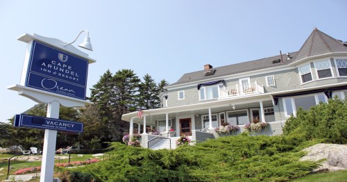 A charming gray inn with a sign reading "Cape Arundel Inn Resort" and lush greenery in front.