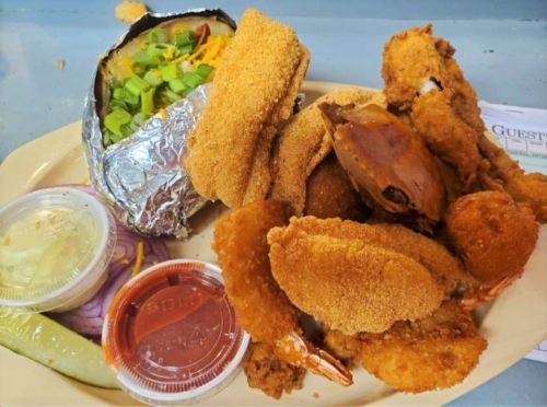 A plate of fried seafood including shrimp, crab, and fish, served with a baked potato and dipping sauces.