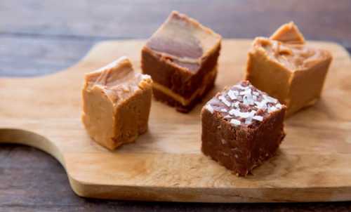 Four pieces of fudge on a wooden cutting board, including chocolate and peanut butter flavors, with one topped with salt.