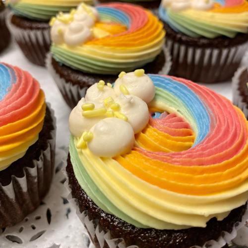 Colorful rainbow cupcakes with swirled frosting in vibrant hues and decorative white icing accents.