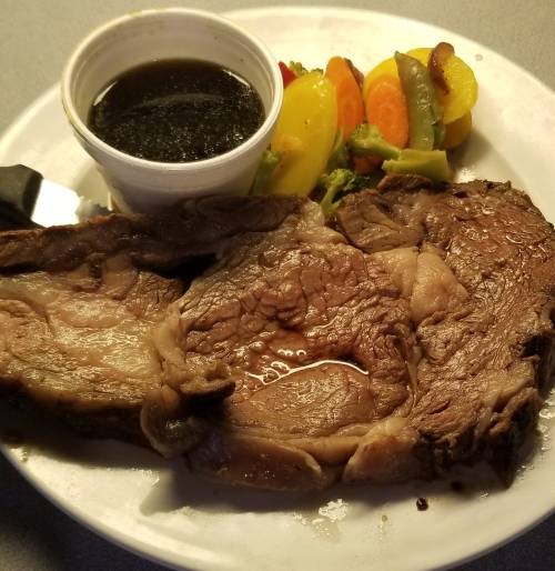 A plate with three slices of juicy roast beef, a small cup of dark sauce, and a side of mixed vegetables.