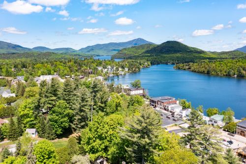 Aerial view of a serene lake surrounded by lush greenery and mountains, with a small town along the shore.