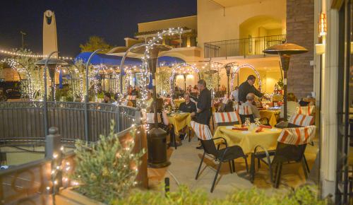 Outdoor dining area at night, with tables set for guests, string lights, and a cozy atmosphere.