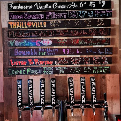 Chalkboard menu displaying various craft beers with prices and descriptions at a bar.