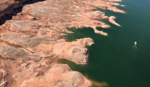 Aerial view of a rocky shoreline with green water, showcasing unique land formations and a small boat in the distance.