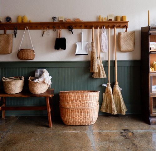 A cozy interior featuring woven baskets, brooms, and a wooden shelf with various tools and decorative items.