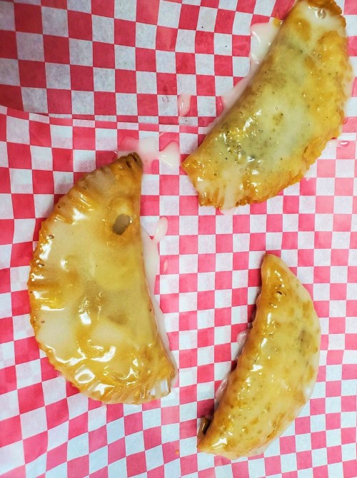 Three golden-brown empanadas drizzled with a sweet glaze on red and white checkered paper.