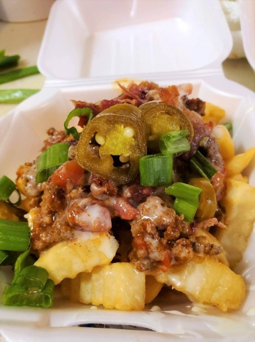 A plate of loaded fries topped with ground beef, jalapeños, tomatoes, green onions, and cheese.