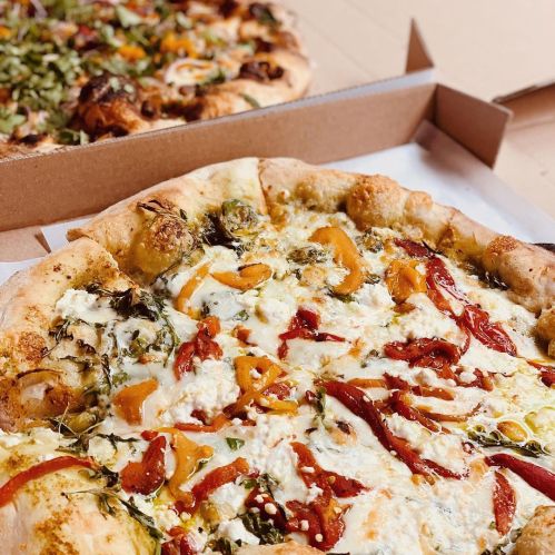 A close-up of a pizza topped with colorful vegetables and drizzled sauces, placed in a pizza box.
