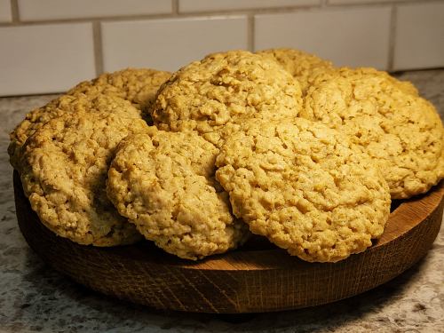 A wooden plate stacked with freshly baked oatmeal cookies, golden brown and textured, against a tiled background.